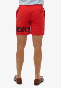 Bañador rojo hecho de material ligero que presenta un gran texto negro "DRY" en la pierna izquierda, cinturilla elástica y un bolsillo trasero.