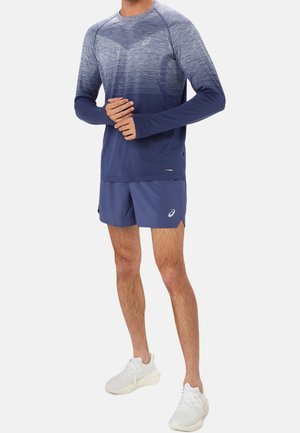 Marineblaues sportliches Langarmshirt mit Farbverlaufstextur, kombiniert mit passenden Shorts. Weiße Turnschuhe vervollständigen das Outfit.
