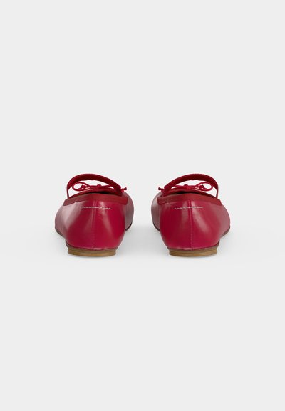 Paire de ballerines rouges avec petits nœuds vues de dos sur un fond clair uni.