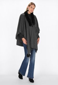 Poncho gri cu un guler din blană sintetică neagră, fabricat din material moale cu un design drapat, asortat cu blugi evazați și cizme negre până la gleznă.