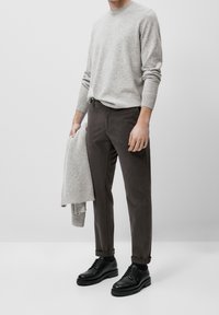 Maglione grigio chiaro in maglia, pantaloni marroni e scarpe di pelle nera. Il maglione ha polsini a coste; i pantaloni sono sartoriali con una texture liscia.