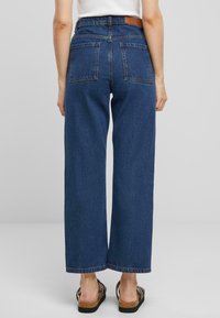 Jeans de denim azul de pierna ancha con una cintura alta, que cuentan con dos bolsillos traseros y un parche de cuero en la cinturilla. Tela texturizada, corte casual.