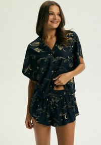 Krótki, granatowy komplet piżamowy ze złotymi wzorami niebiańskimi. Zawiera krótki, zapinany na guziki top z krótkim rękawem oraz szorty z elastycznym pasem. Gładka struktura materiału.