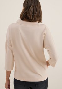 Beige top s tříčtvrtečními rukávy a uvolněným střihem a širokým výstřihem. Měkká textura se hladkým povrchem a minimem švů.