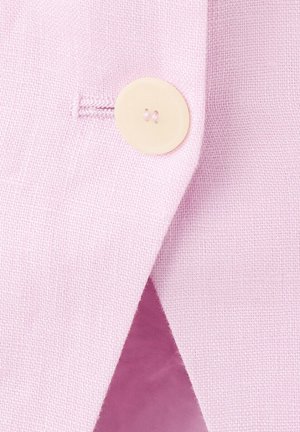 Plano detalle de un botón crema cosido en tela de lino rosa claro con un ojal, resaltando la textura y los detalles de la costura.