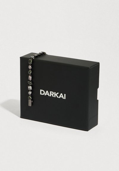 Mustast DARKAI kastist ripub hõbedane ja tume kalliskividega käevõru, mis on valgel pinnal pehme valgustusega eksponeeritud.