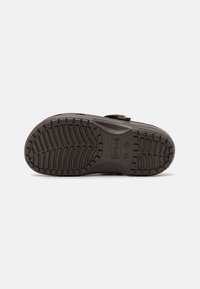 Semelle de chaussure en caoutchouc noir avec des motifs de texture et des points en relief, dotée d'une sangle et d'un logo de marque imprimé sur le côté.