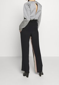 Grå tröja med nyckelhålsdetalj på ryggen, kombinerad med svarta vida byxor som har vertikala ränder i rosa och krämfärg längs sidorna.