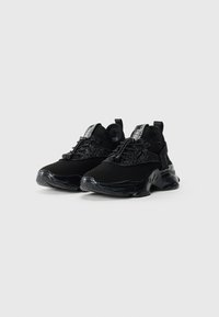 Une paire de baskets de sport noires avec un tissu en maille texturé, des semelles épaisses et rembourrées, et des lacets en élastique à tirette sur un fond blanc.