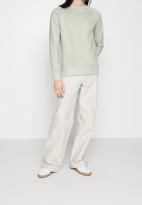 Sudadera de algodón verde claro con cuello redondo y puños acanalados, combinada con pantalones de pierna ancha beige y zapatillas blancas.