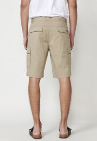 Beige cargo šortky se širokým střihem, dvěma bočními kapsami a jednou zadní kapsou, vyrobené z lehkého materiálu, zakončené ke kolenům.