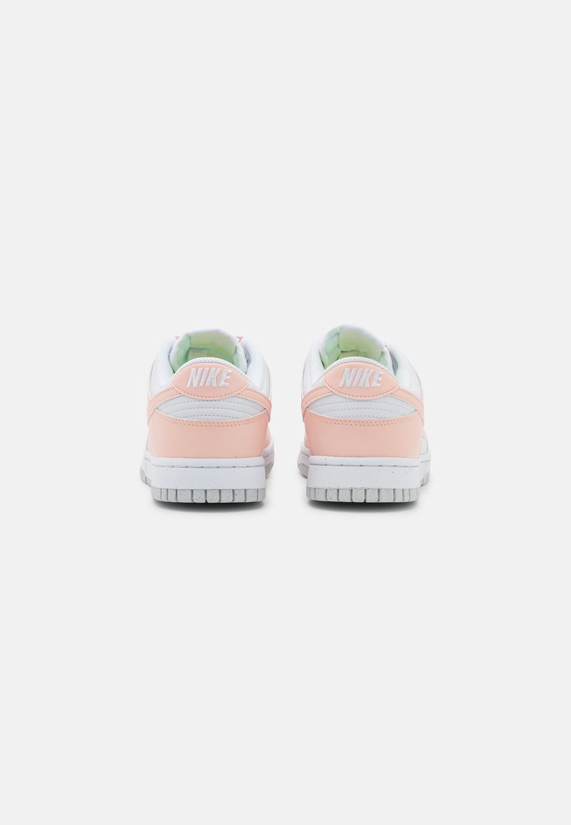 Nike-Sneaker mit weißem Lederobermaterial, pinken Akzenten und grauer Gummisohle. Verfügt über einen gepolsterten Kragen und eine Fersenlasche mit Logo.
