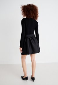 Top preto de mangas longas com tecido texturizado e design ajustado, combinado com uma saia preta de evasé com cintura franzida e detalhes brilhantes.