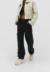 Cropper beige shearling jakke med sorte cargo bukser. Beige sneakers. Jakken har lynlås lukning og overdimensionerede manchetter; bukserne har sidelommer.