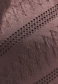 Strukturiertest lila Gewebe mit erhabenen Mustern und Netzakzenten, das eine visuell markante Oberfläche mit unterschiedlichen Dichten schafft.