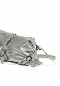 Sac à main en cuir argenté avec des sangles réglables à boucle et des détails en métal en forme d'anneau en D sur fond blanc.