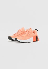 Nike tenisice u svijetlo ružičastoj boji s teksturiranim mrežastim gornjištem, crnim gumiranim potplatom i bijelim međuplatnom. Imaju istaknute vezice i brendirane detalje.