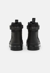 Černé kotníkové boty s hladkým, matným povrchem, s dvojitými řemínky a silnou gumovou podrážkou s texturovanými liniemi.
