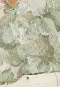 Floral blouse in soft greens and pinks, with a striped texture and small reflective dots. Features button front and short sleeves.