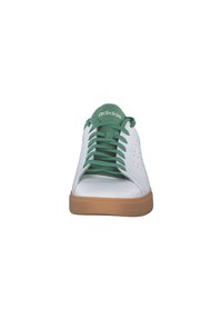Zapatilla blanca con cordones y acentos verdes. Presenta una parte superior de cuero suave, perforaciones en los laterales y una suela de goma marrón.