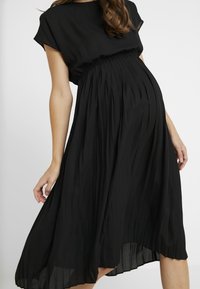 Musta poimutettu mekko rentoa leikkausta, lyhyet hihat ja elastinen vyötärö. Kevyt kangas laskeutuu kauniisti keski-pohkeeseen.