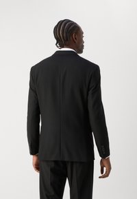 Schwarze Anzugjacke mit taillierter Passform, einfacher Schlitze und vierknöpfigen Manschetten, unter der eine klassische weiße Hemd getragen wird.
