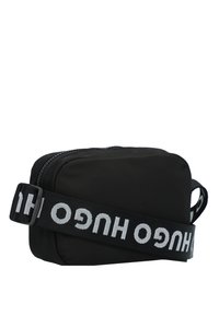 Borsa a tracolla nera in nylon con chiusura a zip, dotata di una tracolla testurizzata contrassegnata con "HUGO" in lettere bianche. Forma rettangolare compatta.