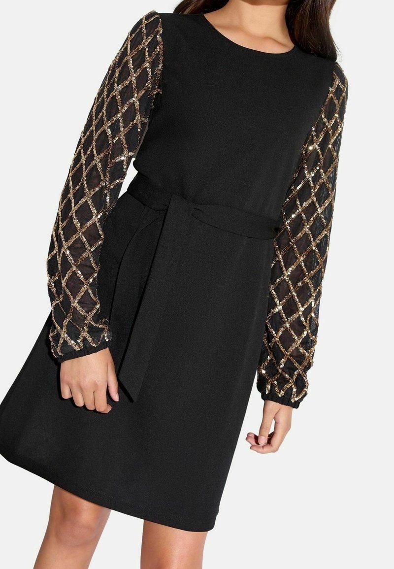 Robe noire avec de longues manches transparentes présentant un motif losange en sequins dorés et une ceinture en tissu noir assortie à la taille.