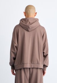 Overdimensioneret brun hoodie lavet af blødt stof, med hætte, sænkede skuldre og ribbede manchetter. Glat tekstur med en afslappet pasform.