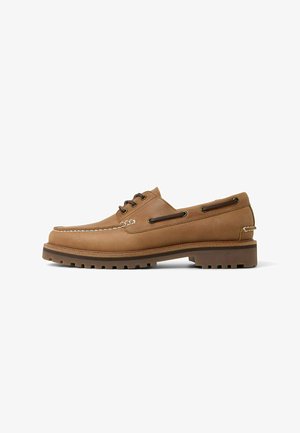 Bateaux en cuir marron avec un design à bout moc, des coutures blanches contrastantes, des œillets en métal et une semelle en caoutchouc texturée.