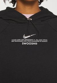 Svart huvtröja gjord av mjukt tyg, med en silverfärgad Nike-logga, vit text och en dragsko med en metallaglet.