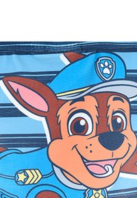 Postać z kreskówki przedstawiająca brązowego psa w niebieskim mundurze policjanta i czapce, z przyjaznym wyrazem twarzy, na niebieskim tle.