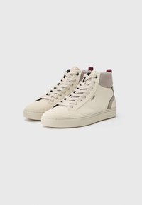 Een paar beige hoge sneakers met witte veters, een mesh enkelkraag, bordeauxrode trekkoorden en het "HUGO"-logo op de zijkant.