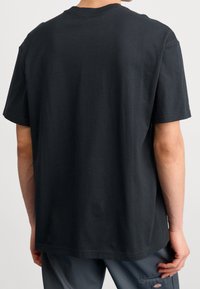 Svart bomullströja med en avslappnad passform, korta ärmar och rundad halsringning. Baksidan har en jämn textur, utan synliga mönster eller designer.