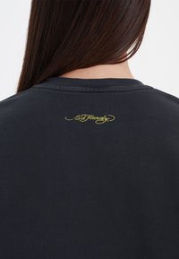 Zwarte sweatshirt met een geribde halslijn en het geborduurde "Ed Hardy" logo in het geel op de bovenrug. Soepele textuur, casual ontwerp.