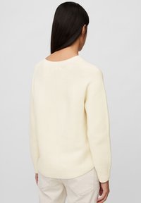 Cremefarbener Strickpullover mit rundem Ausschnitt und langen Ärmeln. Verfügt über ein strukturiertes Muster und eine taillierte Passform im Rücken.