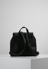 Mochila de cuero negro con diseño estructurado, asa superior, correas de hombro ajustables y textura suave. Presenta una apariencia elegante y minimalista.