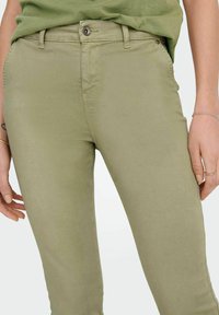 Olivově zelené chinos ve slim střihu vyrobené z měkké, elastické bavlny. Mají přední zapínání na knoflík a nenápadné boční kapsy. Hladká struktura.