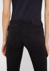 Svarta denimjeans med en åtsittande design, som har distinkta bakfickor och en texturerad läderetikett vid midjan.