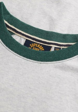 Tæt på en lysegrå sweatshirt-udskæring med en mørkegrøn ribkant og et synligt Superdry-mærke indeni.