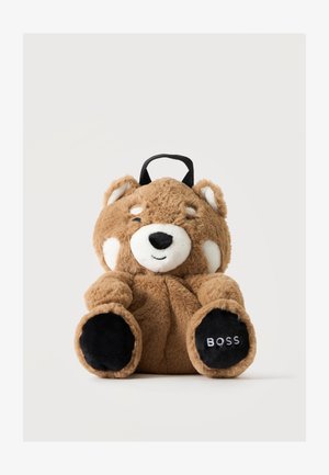 Zaino orso marrone in peluche con un volto sorridente, segni bianchi sul viso, cuscinetti neri sulle zampe e una maniglia nera nella parte superiore. Su una zampa c'è scritto "BOSS."