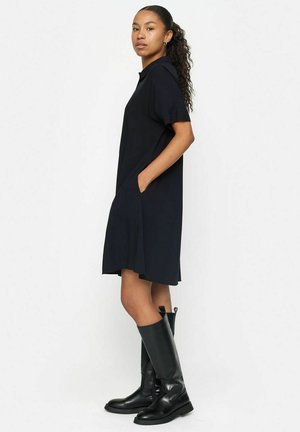 Vestido de manga corta azul marino con cuello de solapa, bolsillos laterales y corte holgado, combinado con botas de cuero negras hasta la rodilla.