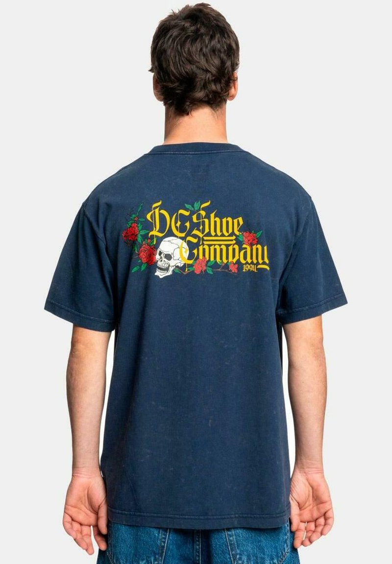 Navy blue cotton t-shirt featuring a large graphic on the back with a skull, roses, and the text “DC Shoe Company” in yellow.