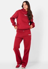 Rode sweatshirt en bijpassende joggingsbroek van zachte stof. Met capuchon, voorkant met zak en witte logotekst. Relaxte pasvorm.