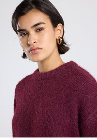 Burgundy knitted sweater with a crew neckline and textured fabric. Features a relaxed fit and soft, fuzzy appearance.