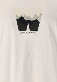 Vit T-shirt med en grafik som visar bokstaven "W" och en bergdesign i svart och ljusa färger, texten lyder "UTOMHUSENTUSIAST."