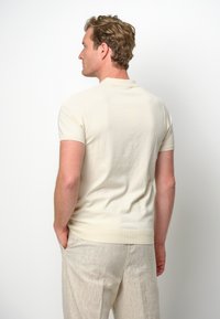 Kortärmad, beige polo-tröja i mjukt material, med klassisk krage och ribbade mudd, i kombination med lätta linnebyxor.