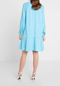 Ljusblå klänning med långa ärmar, samlad fåll och en avslappnad passform. Tillverkad av mjukt tyg, med rund halsringning och knäppta manschetter.