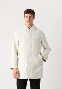 Abrigo impermeable de color beige claro con corte recto, cuello plano, botones frontales, mangas largas y bolsillos laterales; textura suave.