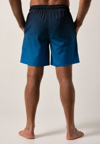 Modré plavky s gradientním efektem, mají elastický pas a boční kapsy. Materiál se zdá být lehký a rychleschnoucí.